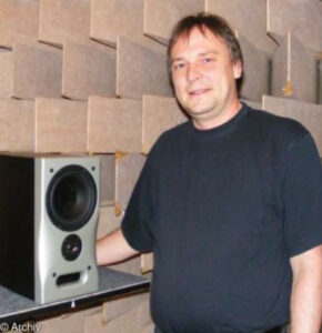 Man standing in front of an acoustic wall panel next to a loudspeaker.