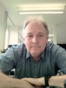 Man sitting at his desk and looking straight into the camera with a friendly face.