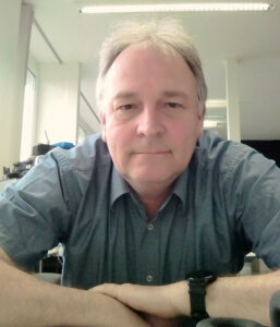 Man sitting at his desk and looking straight into the camera with a friendly face.