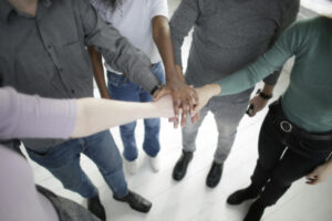 Group of people standing in a half circle putting their hands on top of each other - symbol of team effort.